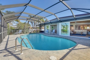 A swimming pool with a covered patio area, lounge chairs, and a view of the surrounding landscape.