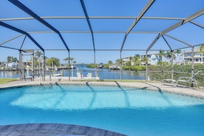A swimming pool with a clear view of the water, surrounded by a covered area with metal beams, and a view of the water body and buildings in the background.