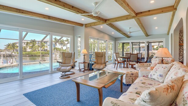 A spacious living area with a glass coffee table, floral sofa, and large windows overlooking a pool. - Waterfront Palmetto Home w/ Private Pool & Dock! (Palmetto)