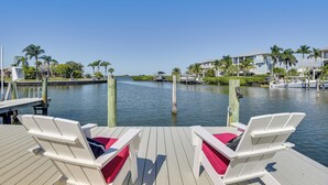 A waterfront deck with two white lounge chairs, a dock, and a marina with boats. - Waterfront Palmetto Home w/ Private Pool & Dock! (Palmetto)
