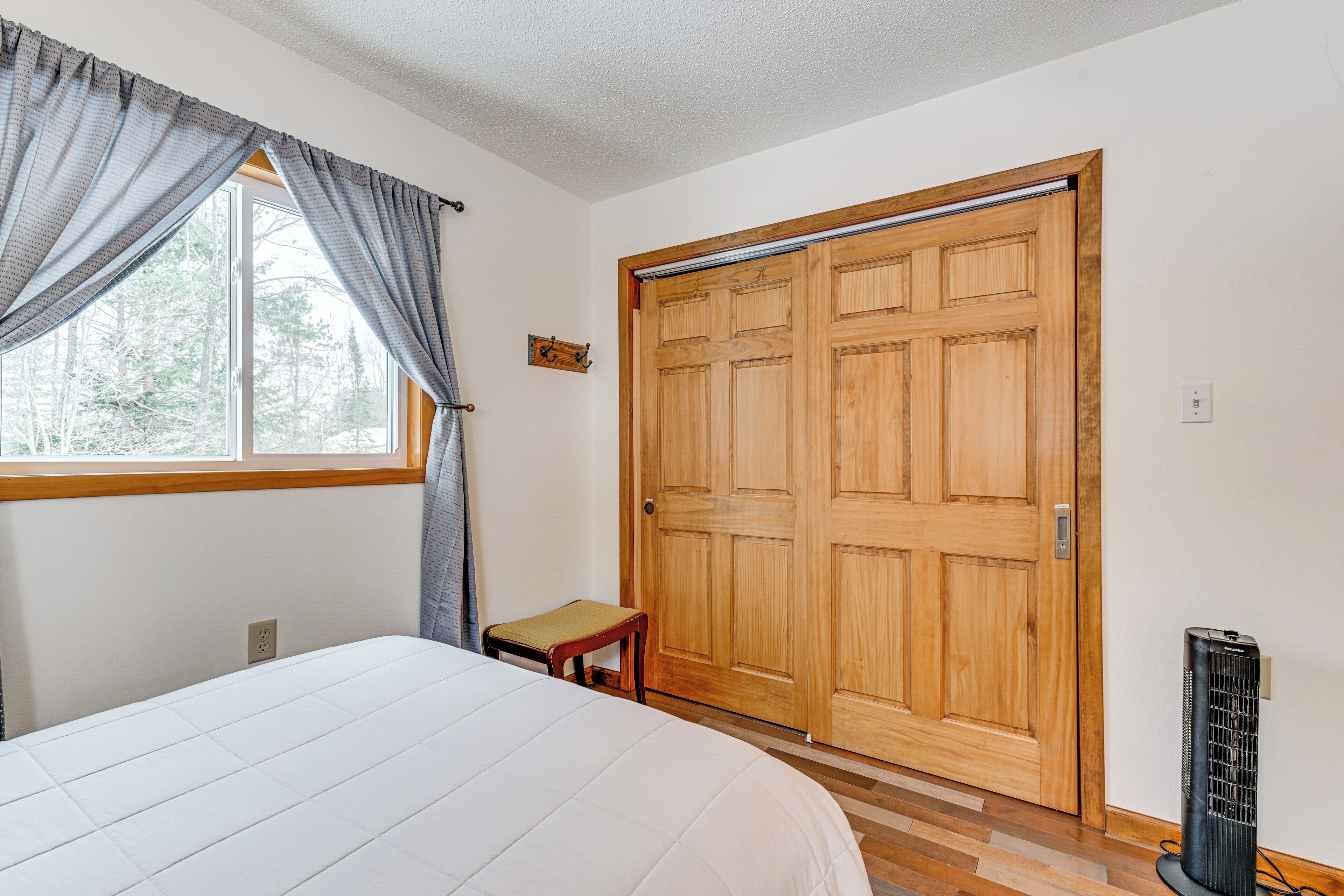 A bedroom with a bed, a wooden wardrobe, a small stool, and a heater.