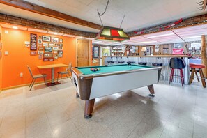 A pool table in a room with orange walls, a wooden ceiling, and a bar area in the background. - Lakefront Suring Home w/ Pool Table + Views! (Suring)