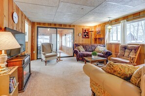 A cozy living room with a sofa, armchair, and a television on a wooden cabinet. - Lakefront Suring Home w/ Pool Table + Views! (Suring)
