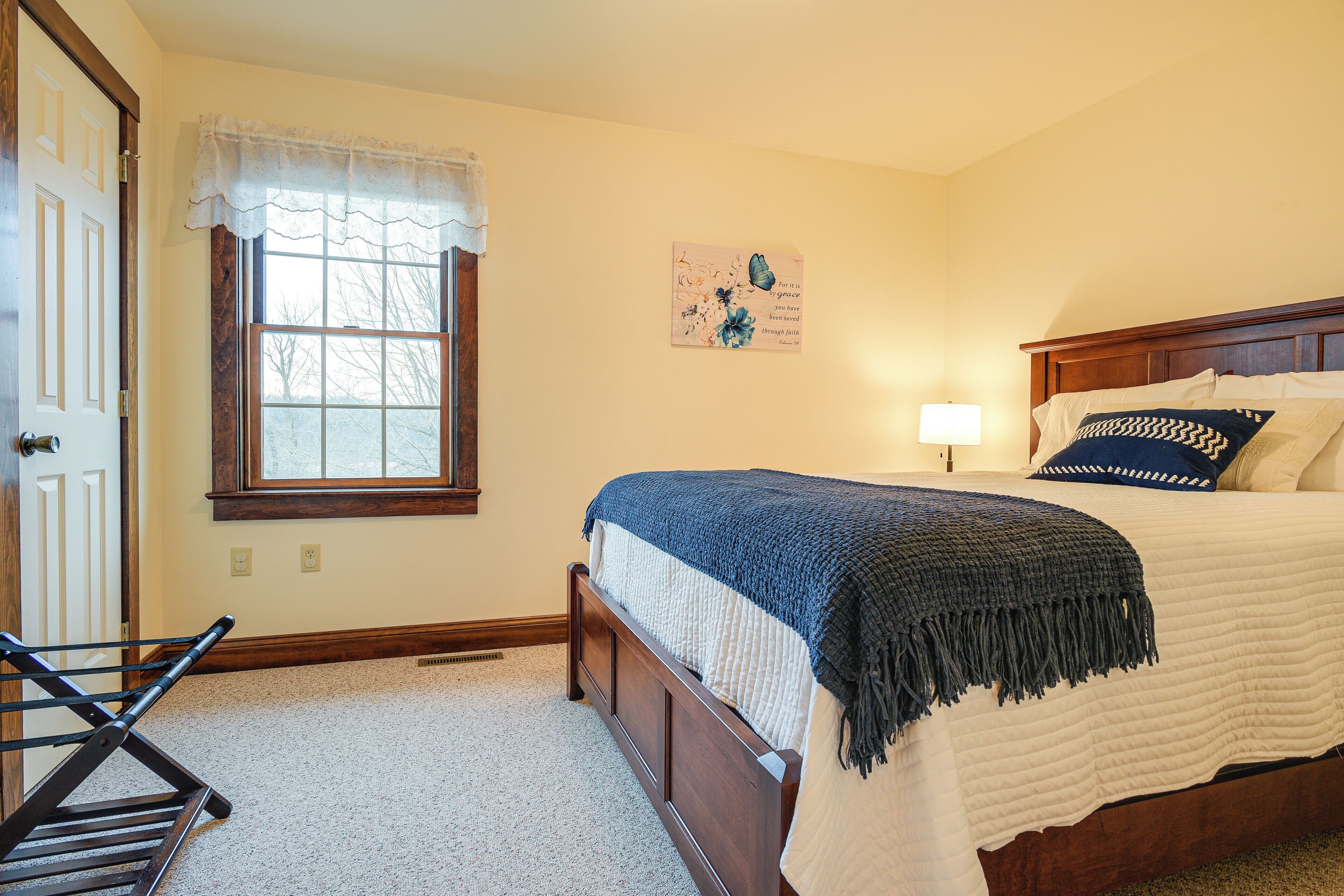 A bedroom with a bed, a window with a curtain, a wall-mounted artwork, and a door.