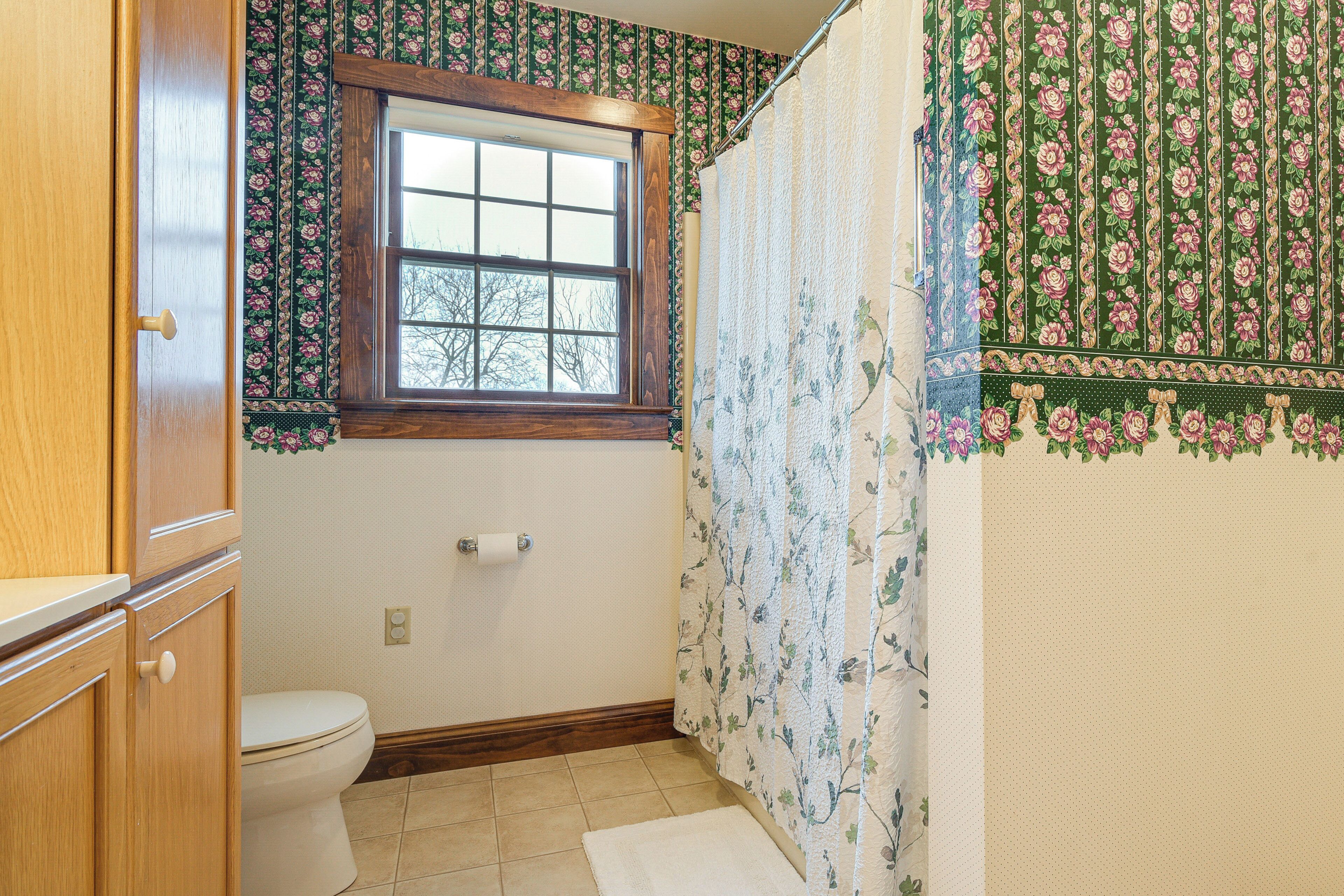 A bathroom with a toilet, a window, and a shower curtain with floral patterns.