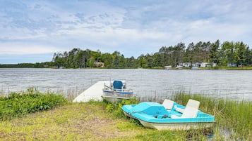 A lakeside scene with two boats docked at a pier, surrounded by lush greenery and a forest in the background.