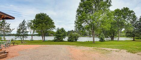 Un espacio con grava, mesas de picnic y una terraza de madera, rodeado de árboles y un lago.
