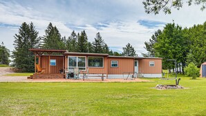 Une cabane en bois d’un seul étage, dotée d’un porche, d’une petite terrasse et d’un foyer extérieur dans la cour.