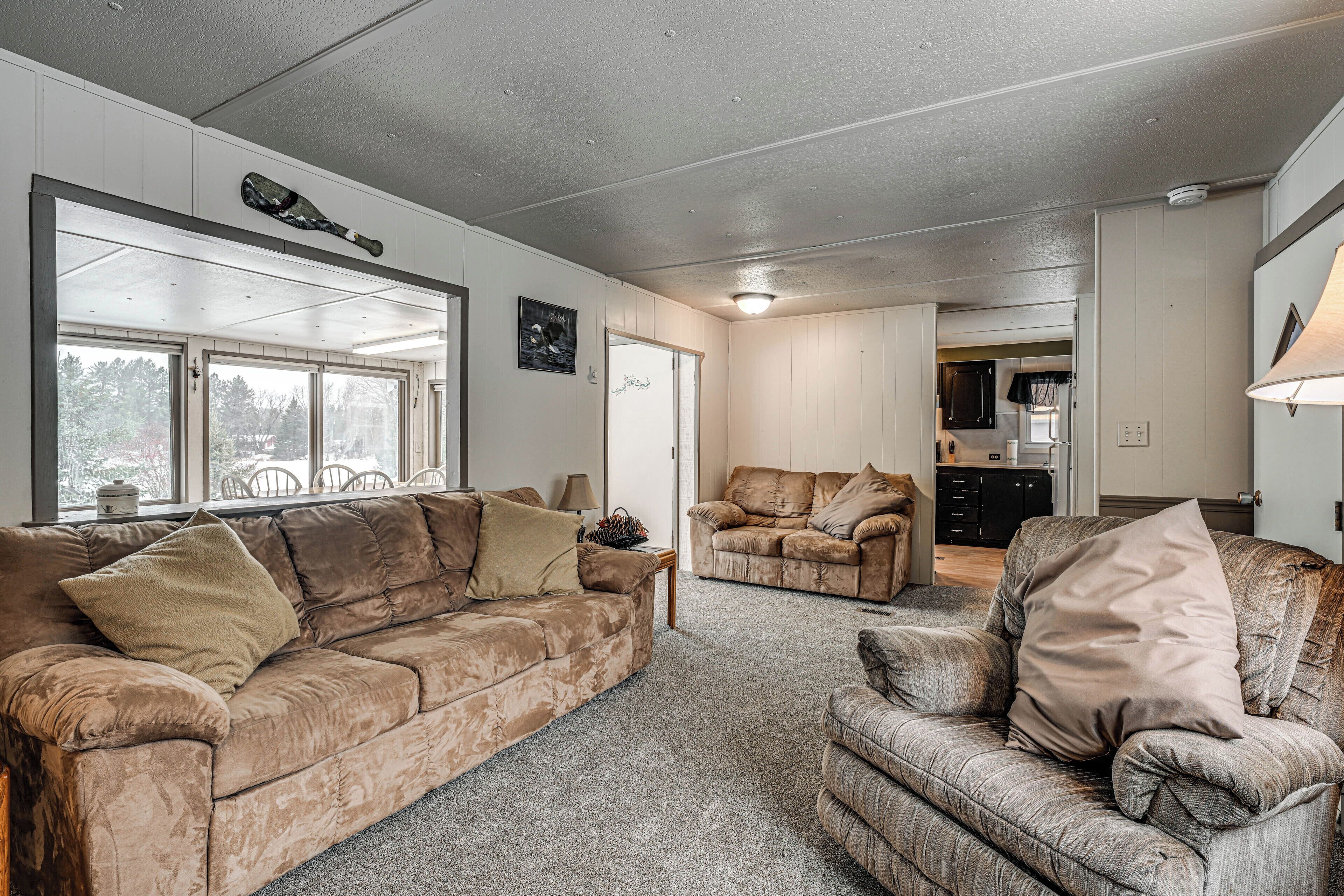 A spacious living room with two sofas and a coffee table, a large window with a view, and a kitchen area in the background.