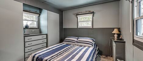 A bedroom with a bed, dresser, window, and lamp.