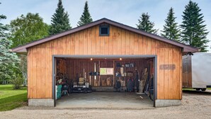Une grange en bois avec une grande porte de garage ouverte, un sol recouvert de gravier et des arbres en arrière-plan.