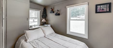 Un dormitorio con una cama grande, una ventana, un pequeño árbol de Navidad y un cuadro en la pared.
