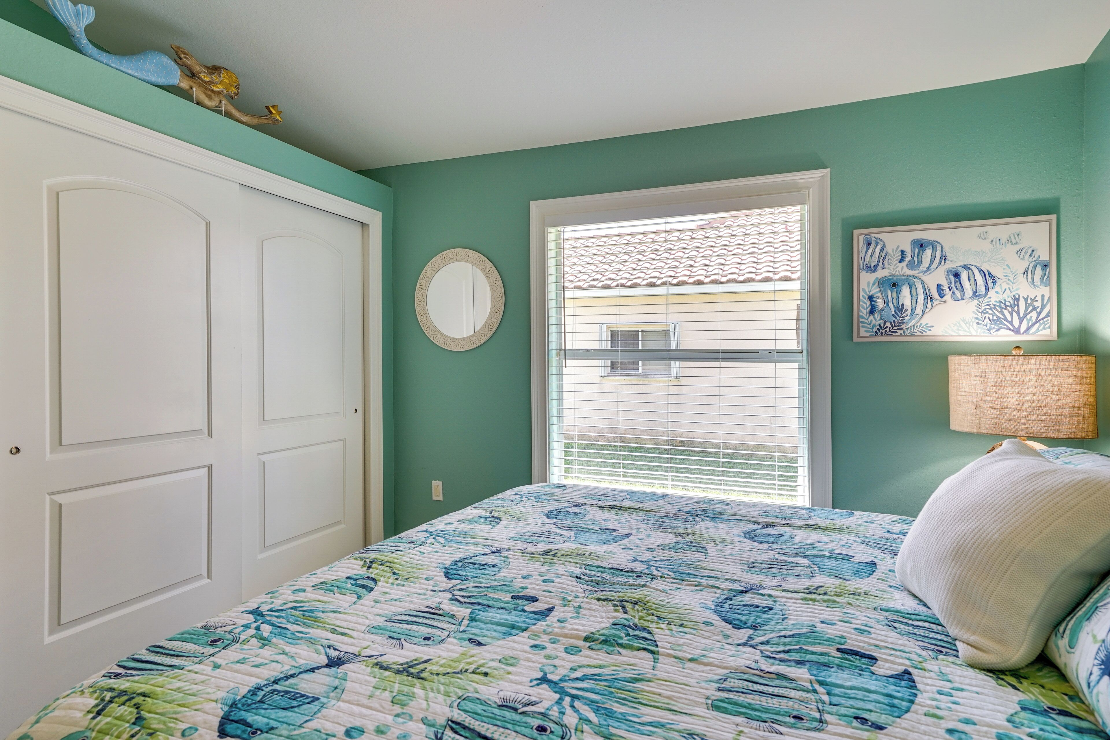 A bedroom with a bed, a window with blinds, a door, and a wall with a framed picture.