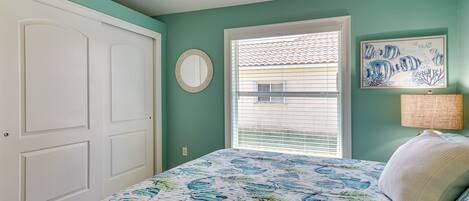A bedroom with a bed, a window with blinds, a door, and a wall with a framed picture.