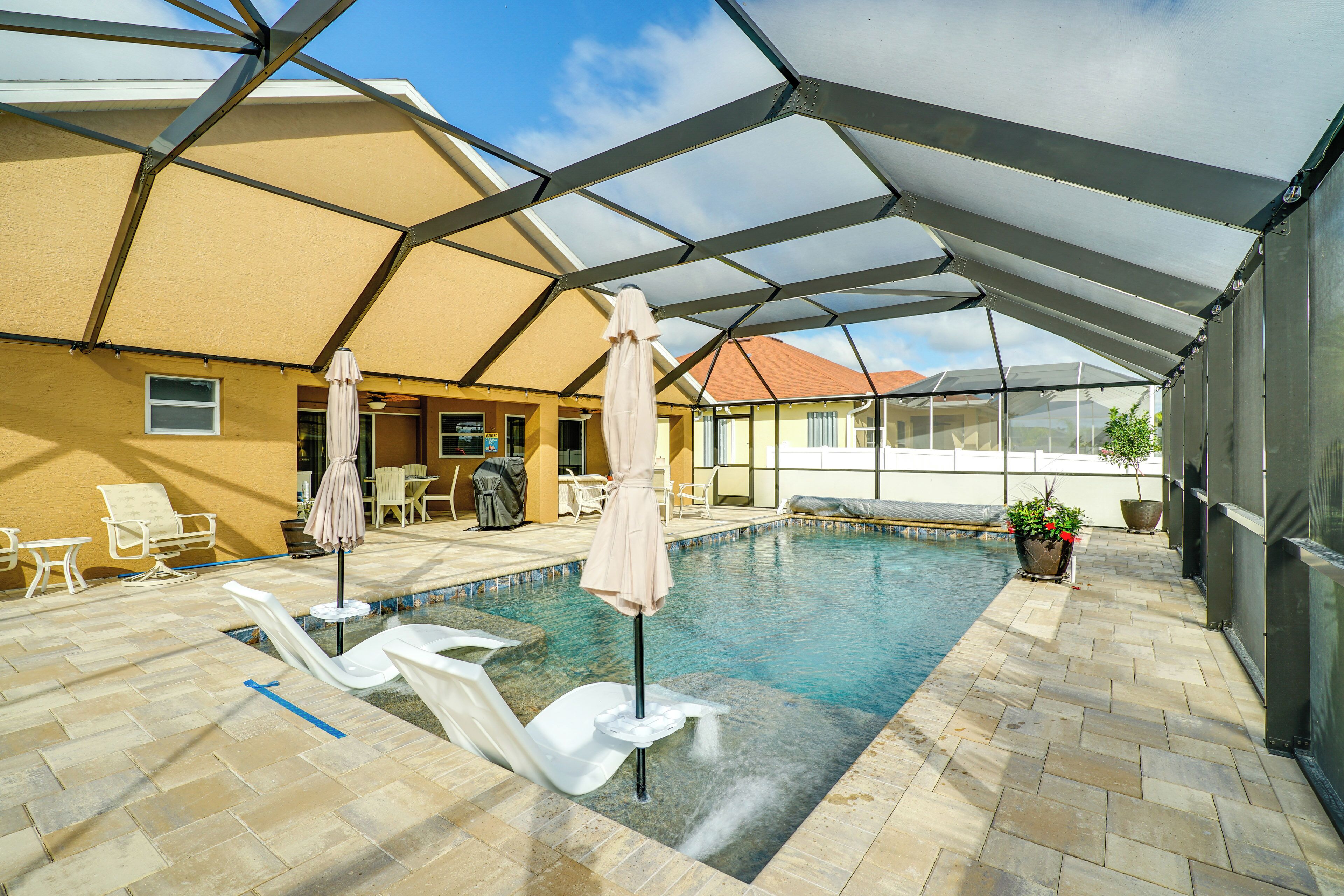 An indoor swimming pool with lounge chairs and umbrellas, surrounded by a covered patio area.