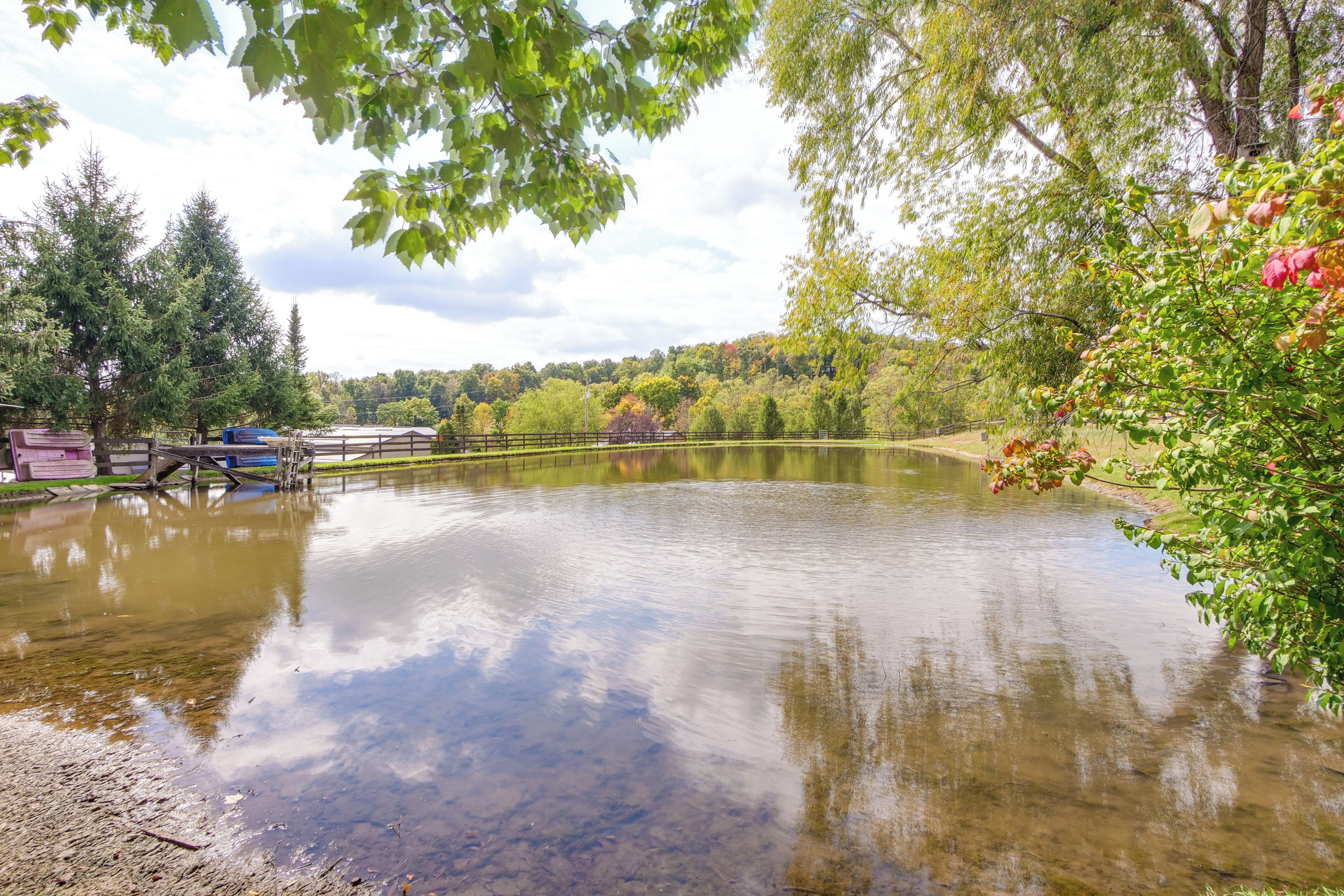 A calm lake with a wooden dock and a bridge, surrounded by trees and a clear sky.