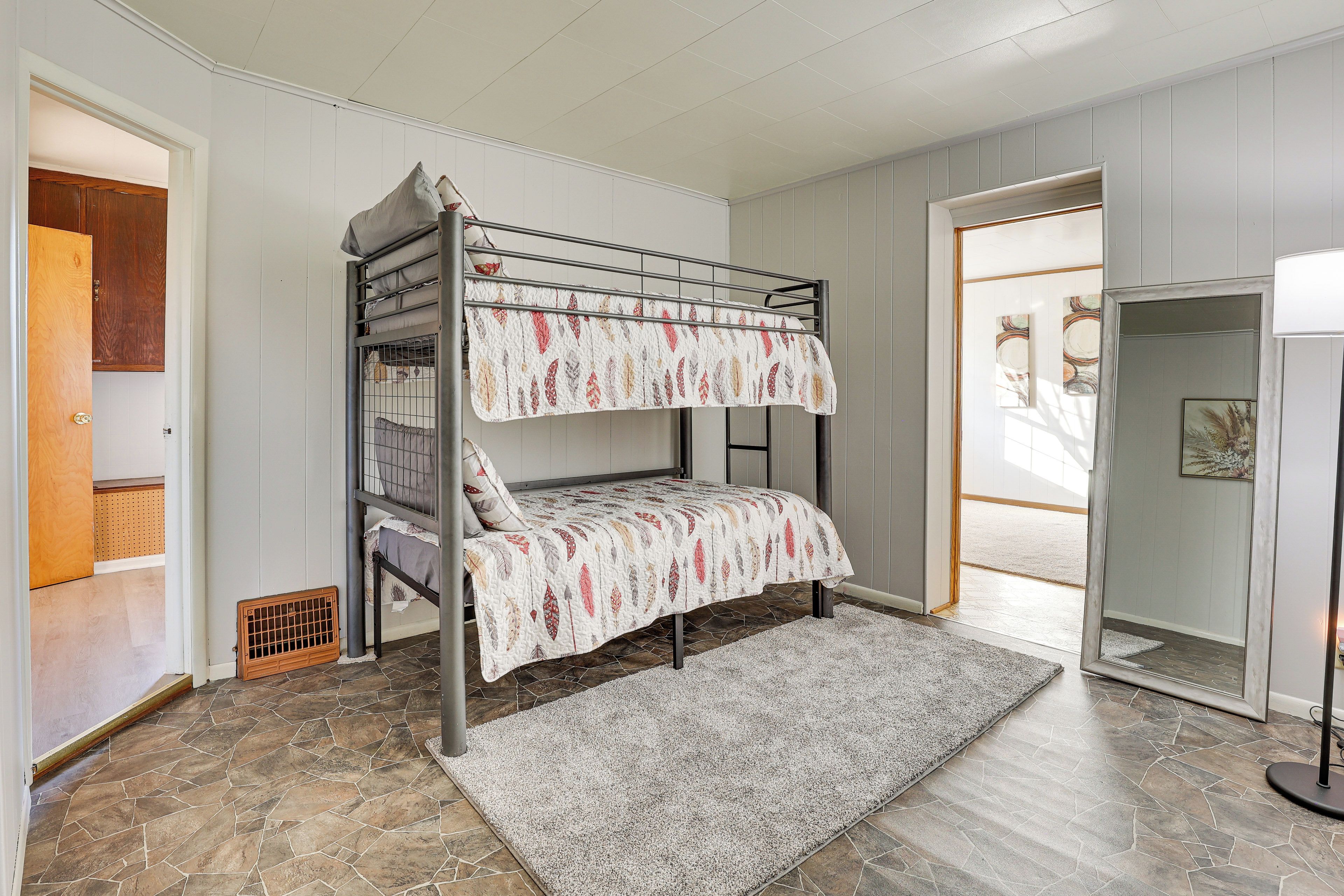 A bunk bed with a patterned bedspread, a stone tile floor, and a gray rug.