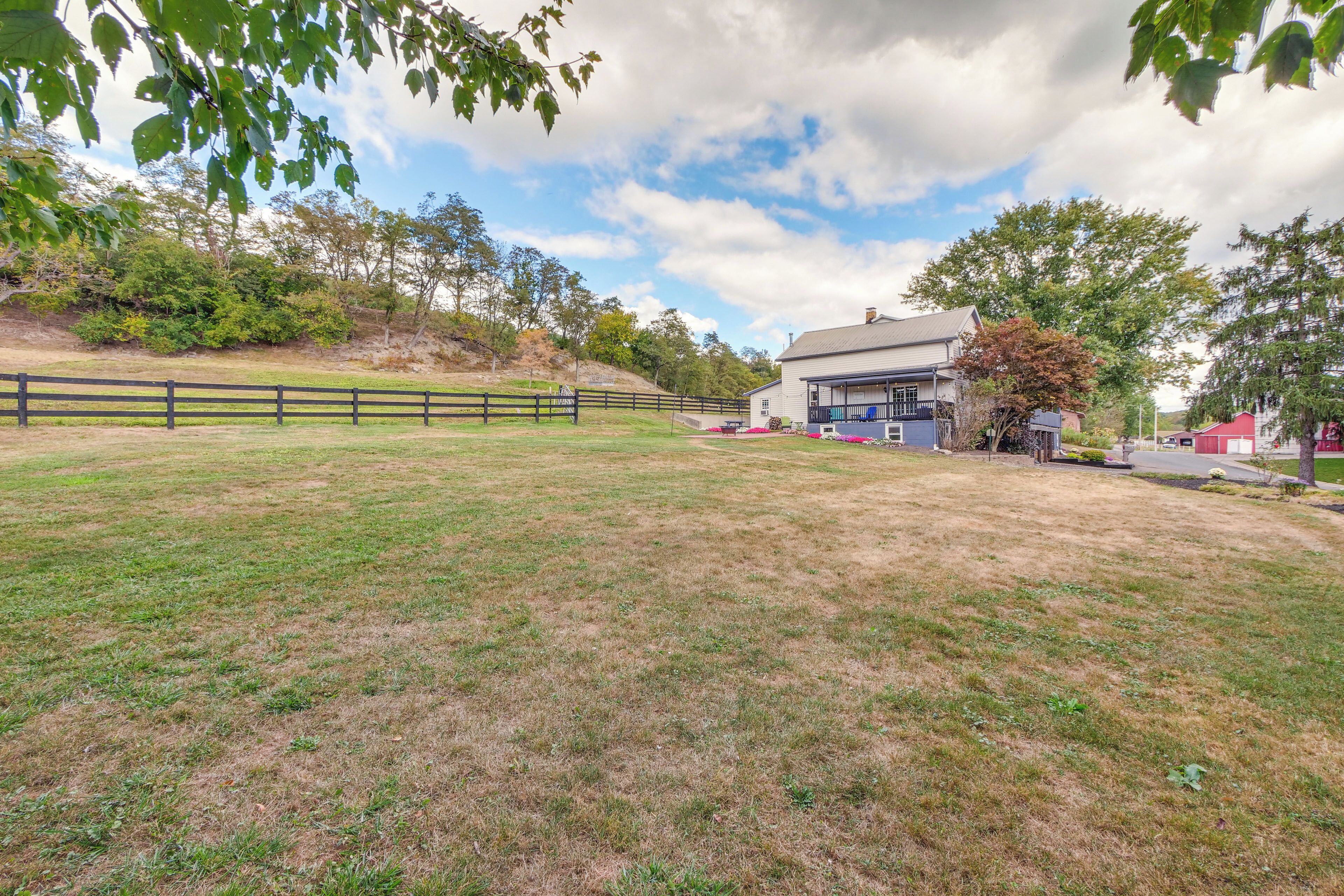 A grassy field with a wooden fence, a house with a porch, and trees in the background.