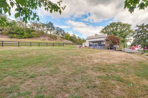 A grassy field with a wooden fence, a house with a porch, and trees in the background. - Farmyard Stays Dundee Home w/ Scenic Views! (Dundee)