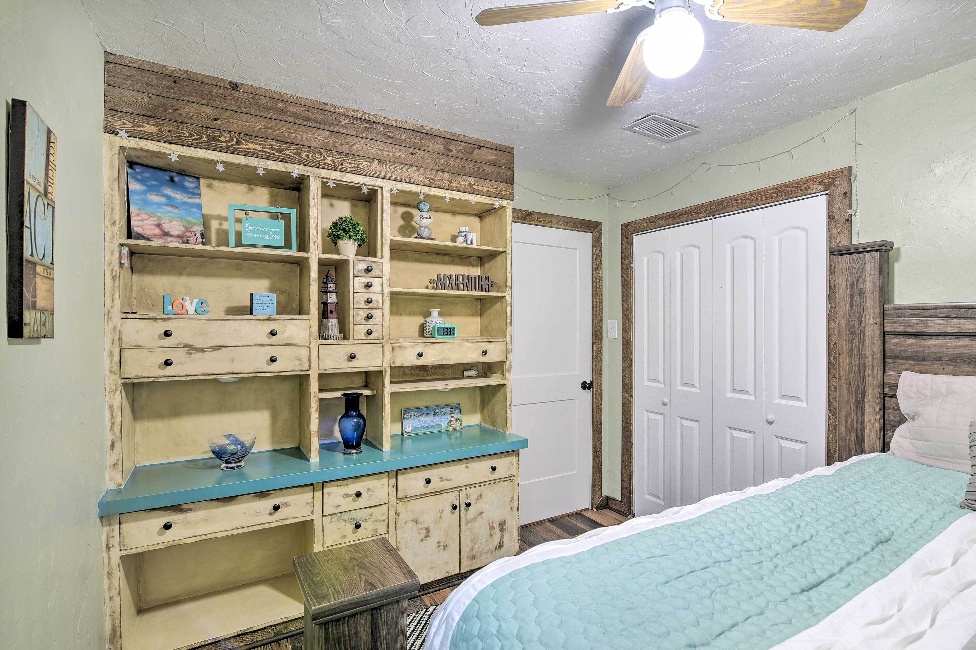 Een slaapkamer met een bed, een dressoir met lades, een wandplank en een deur.