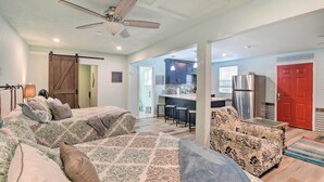 A spacious living area with a large bed, a sofa, and a chair. There is a kitchen in the background with a refrigerator and a red door. - Galveston Group Getaway w/ Private Yard + Fire Pit (Galveston)
