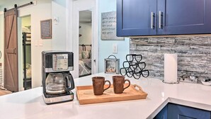 A kitchen with a coffee maker, two mugs on a tray, a wall-mounted towel dispenser, and a sign with a motivational quote. - Galveston Group Getaway w/ Private Yard + Fire Pit (Galveston)