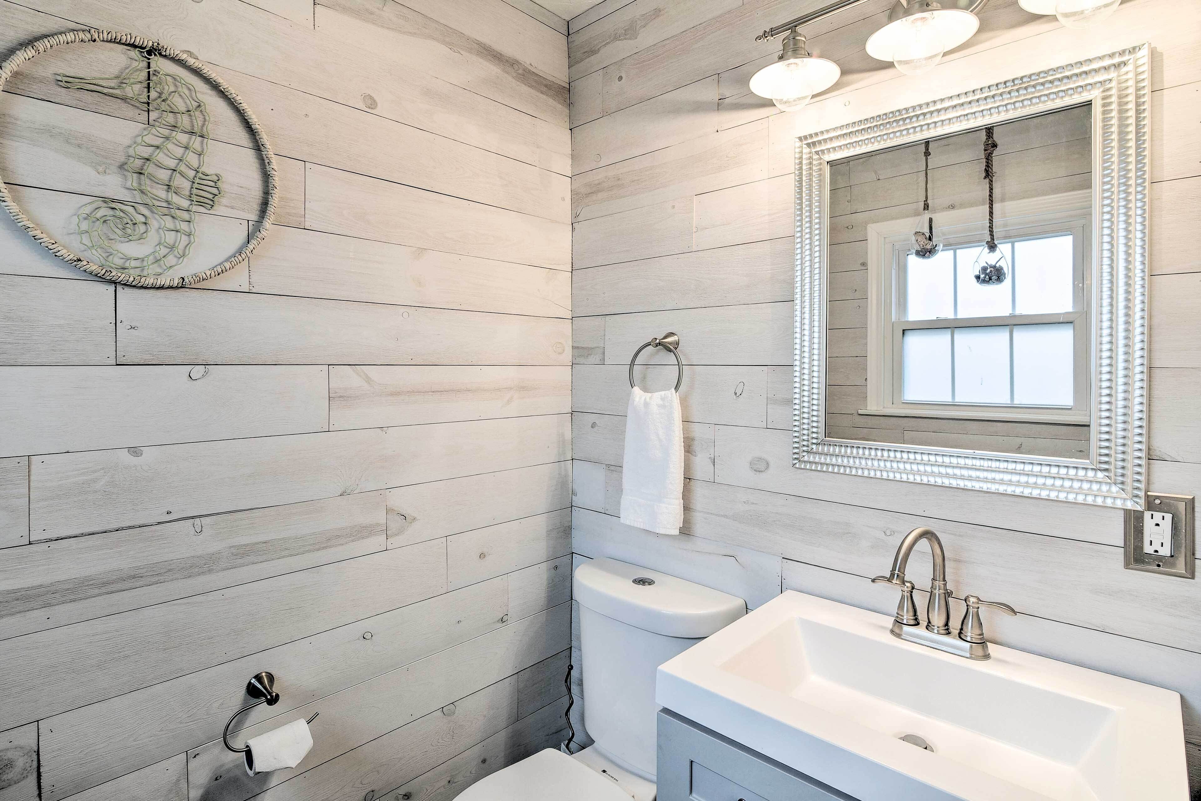 A bathroom with wooden panel walls, a round mirror with a decorative frame, a white sink, and a toilet.