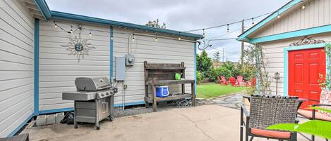 A patio with a grill, outdoor furniture, and a red door in the background.
