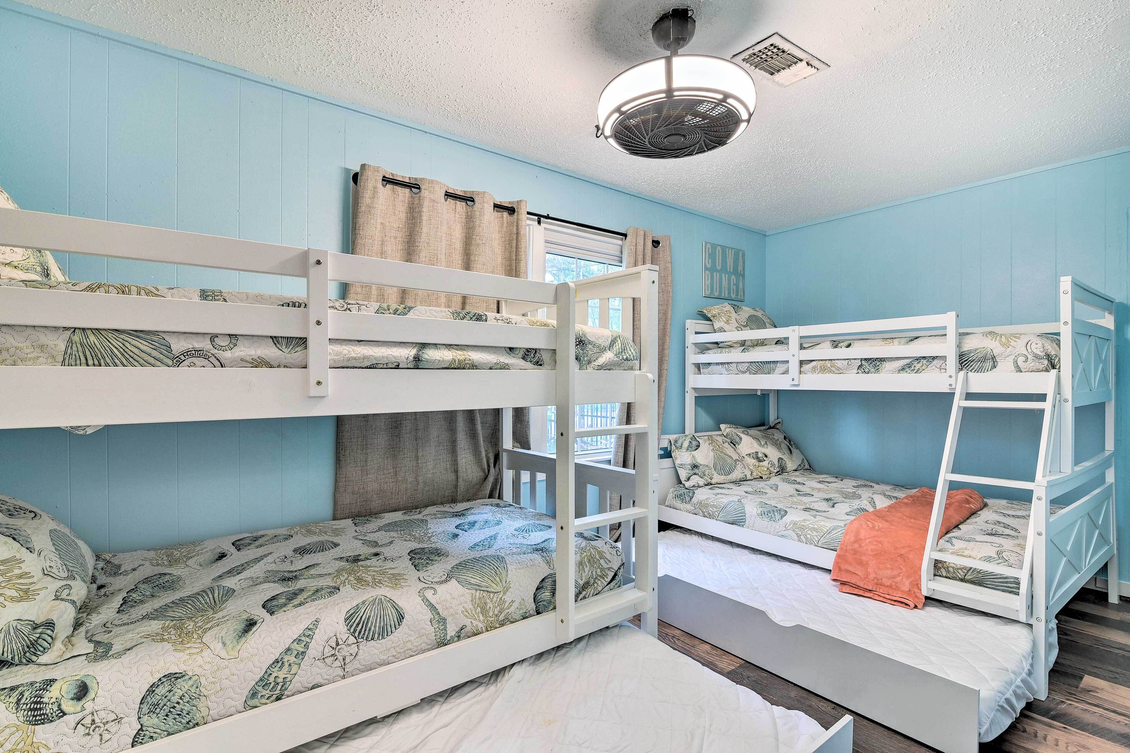 A room with bunk beds, a ceiling fan, and a window with curtains.