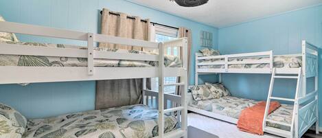 A room with bunk beds, a ceiling fan, and a window with curtains.
