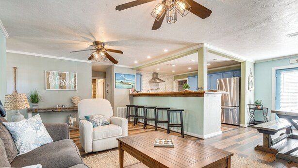 A spacious living room with a wooden coffee table, a white sofa, and a ceiling fan. - Galveston Group Getaway w/ Private Yard + Fire Pit (Galveston)