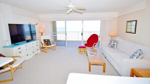 A spacious living room with a television, a red chair, a white sofa, and a balcony with a view. - Beachmark 4k 1 Bedroom Condo by RedAwning (Ocean City)