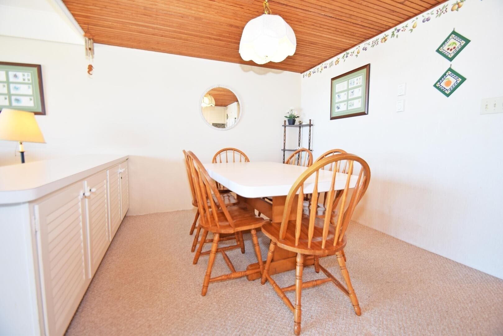 Comedor con una mesa blanca y sillas de madera, una lámpara en el techo y un espejo en la pared.