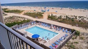 A pool area with lounge chairs and umbrellas, surrounded by a sandy beach and ocean view. - Beachmark 4k 1 Bedroom Condo by RedAwning (Ocean City)
