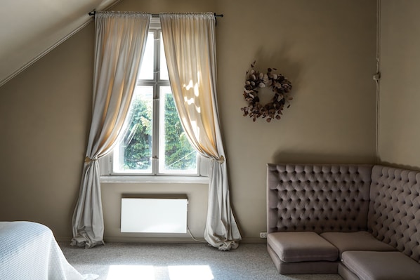 Una habitación con un ventanal grande, un sofá tapizado de gris y una cama blanca.