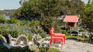 Un banc et une chaise rouges sur une terrasse en pierre, avec une structure au toit rouge en arrière-plan.