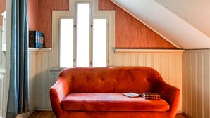 A red velvet sofa in a room with wooden walls and a sloped ceiling. - Topfloor apartment in historic villa - seaview (Vestland)