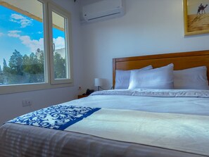 A hotel room with a bed, a window, an air conditioner, and a painting on the wall. - Royal Crown Hotel Giza Pyramids View (Giza)