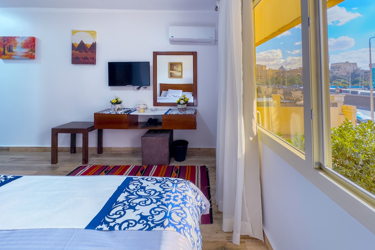 A hotel room with a bed, a desk with a chair, a TV, and a window with a city view.