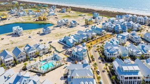 Vue aérienne d’un quartier résidentiel situé sur la côte, avec de nombreuses maisons, une piscine et une plage.