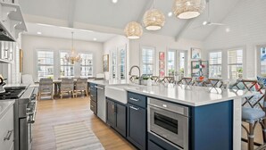 Une cuisine moderne dotée d’un grand îlot central, d’appareils électroménagers en acier inoxydable et de luminaires suspendus.