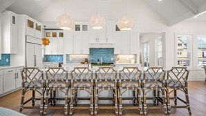 Une cuisine spacieuse avec des meubles blancs, un îlot central et trois lampes suspendues.