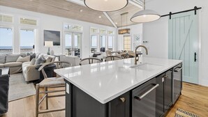 Una cocina amplia con una isla grande, elegantes lámparas colgantes y vistas al océano.