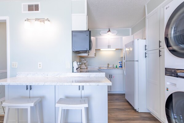 A modern kitchen with white cabinetry, a marble countertop, and a built-in washing machine. - 5th Floor @ World Famous Summit in PCB! (Panama City Beach)