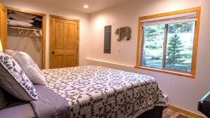 Un dormitorio con cama, armario, ventana con vistas a árboles y estante fijado a la pared.
