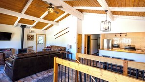 Amplia sala de estar con techo de madera, chimenea, sofá y zona de cocina con electrodomésticos modernos.