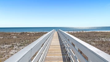 Una pasarela de madera que lleva a la playa, con barandas blancas.