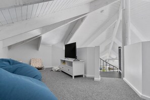 Relax in this stylish loft-style bedroom with a large flat-screen TV, comfortable seating, and a staircase leading to an outdoor area.