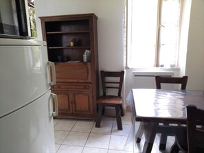 A kitchen with a refrigerator, wooden cabinet, and a dining table with chairs. - LA CHAZOTTE HUT (Bussière-Dunoise)