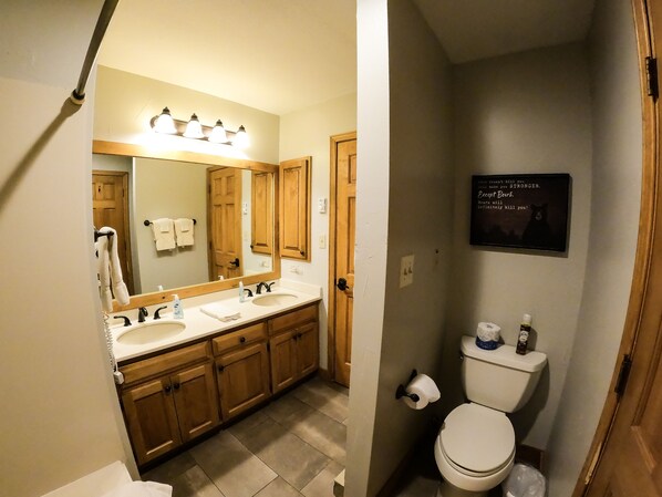 A bathroom with a large mirror, two sinks, wooden cabinets, a toilet, and a motivational quote on the wall. - Studio Loft - Kitchenette, King bed ! (Durango)